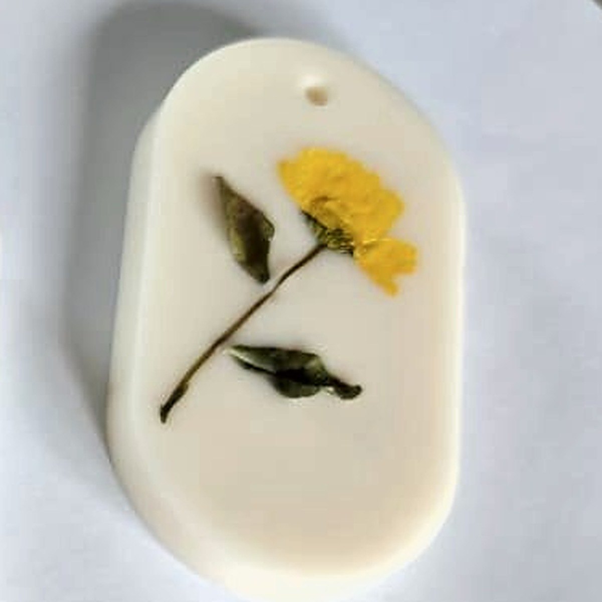 White oval Botanical Wax Tag with a pressed yellow flower and leaves, close view